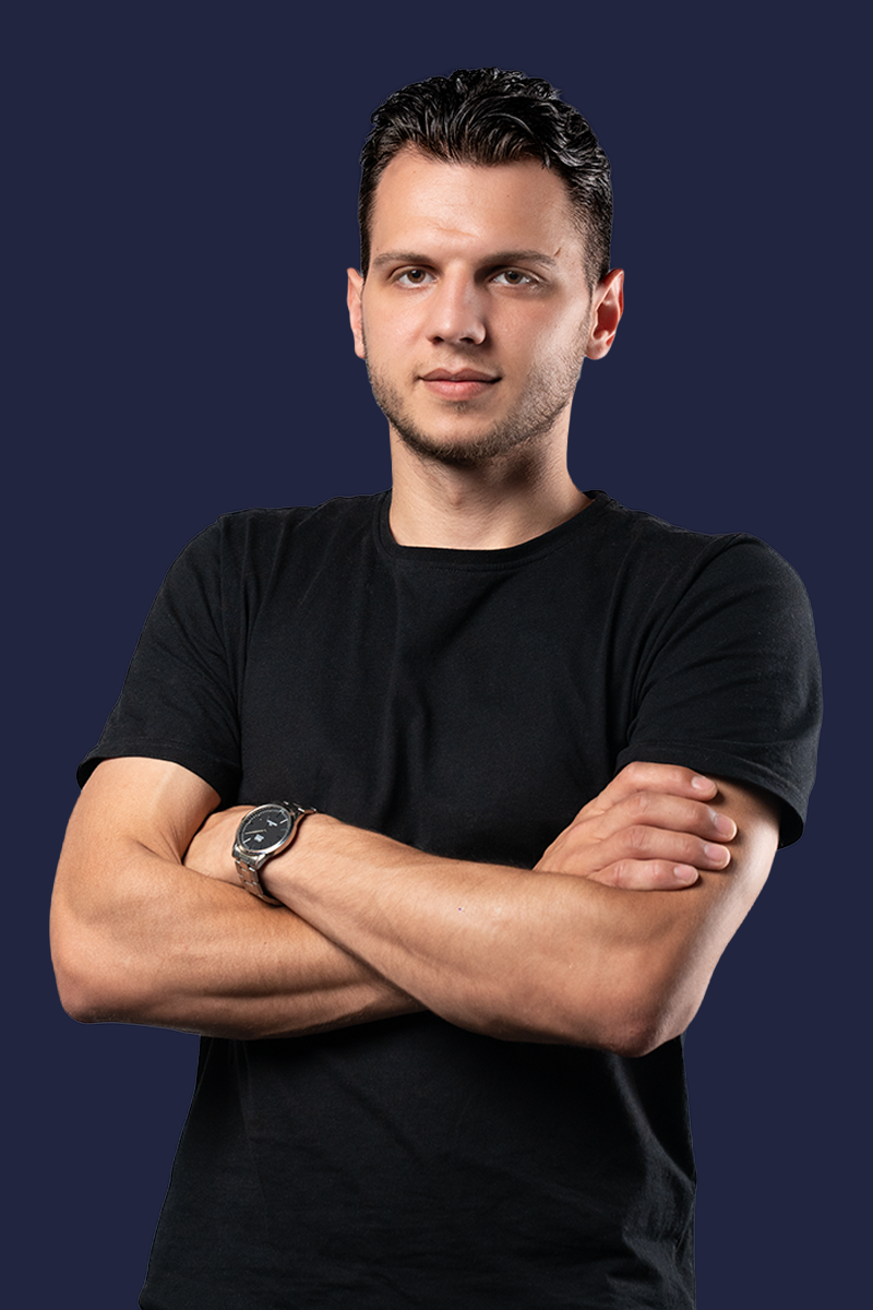 Young man with short hair wearing a black t-shirt and watch, arms crossed, on dark blue background.